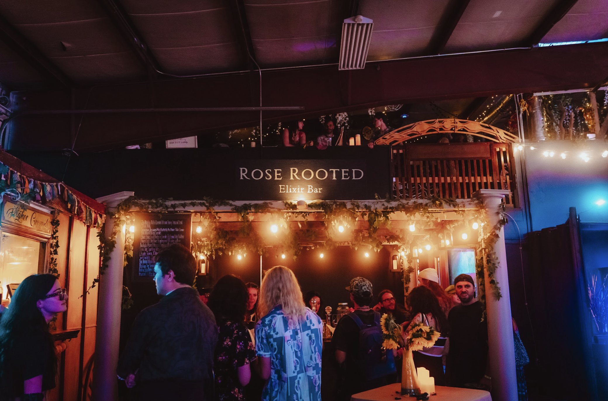 Crowd gathered under string lights at the Rose Rooted Elixir Bar inside The Haven PDX during a First Friday event